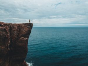 faceless hiker on steep rock over bay under overcast sky