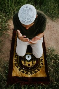 faceless man praying on carpet in field