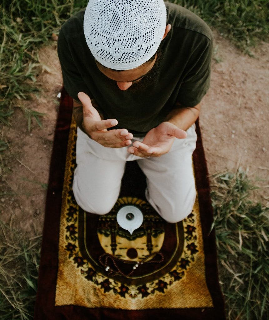 faceless man praying on carpet in field