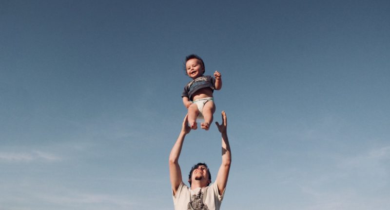 photo of man in raising baby under blue sky
